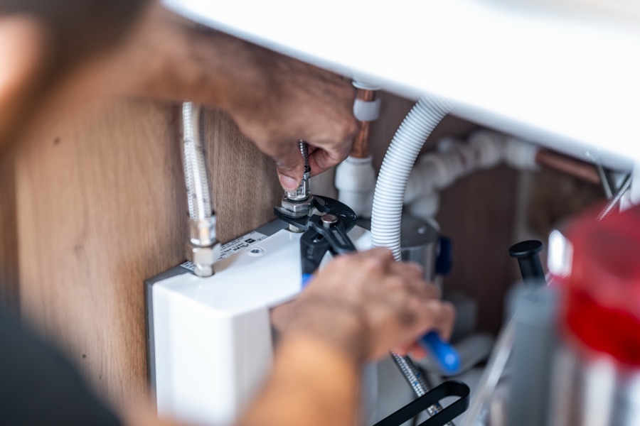 An apprentice fitting a tap under a sink, the kind of job that builds the portfolio